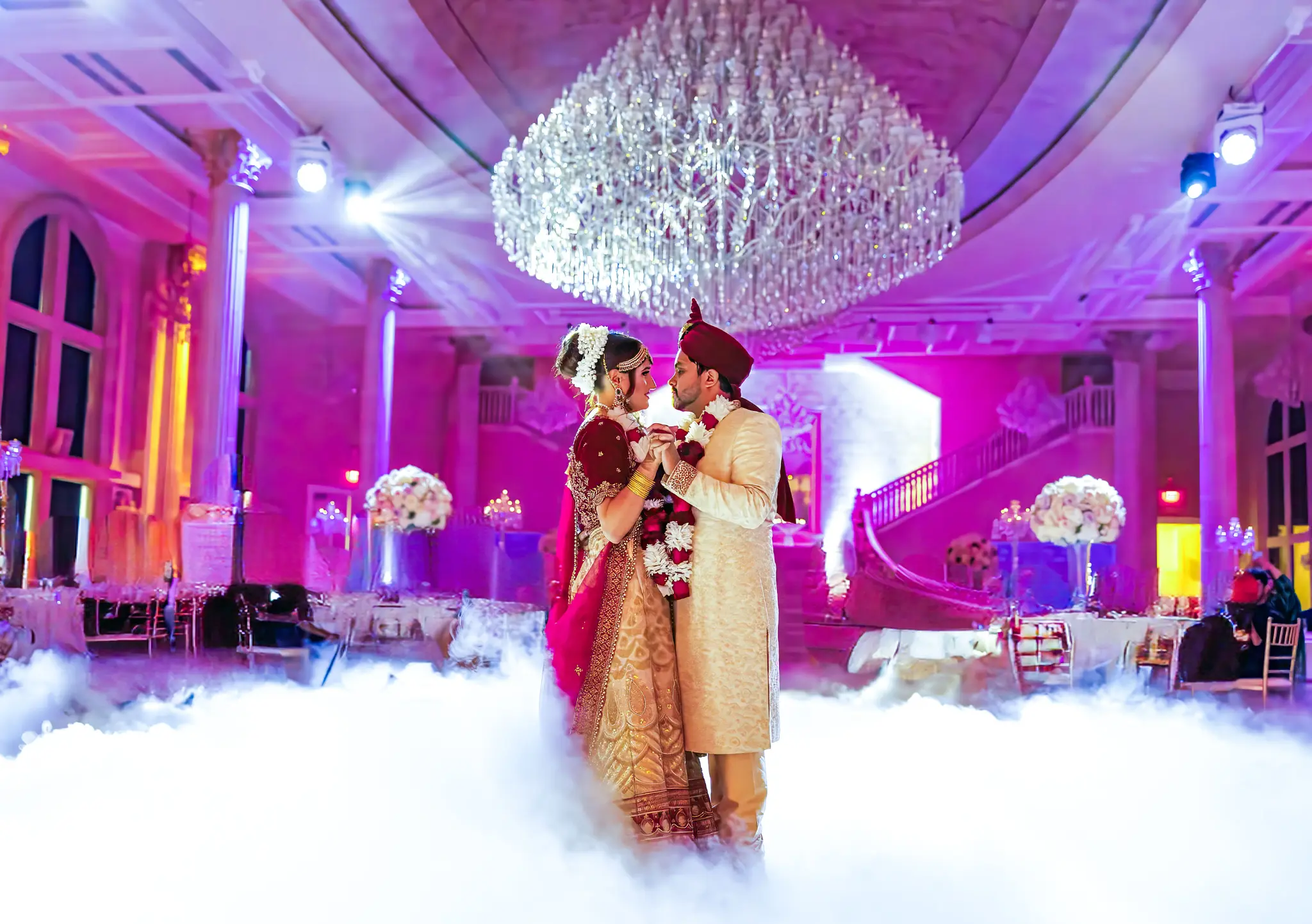 South Asian couple first dance under grand chandelier in luxury ballroom