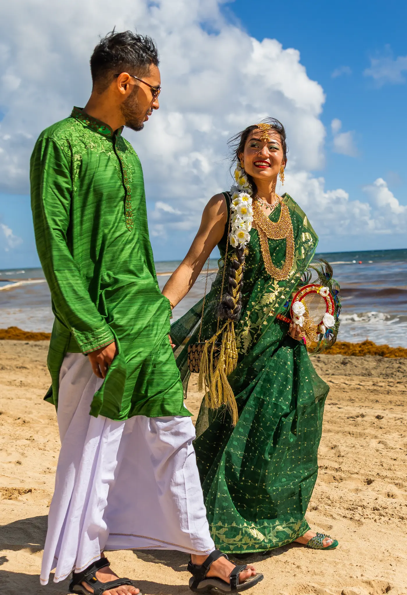 South Asian couple in traditional green attire walking hand in hand on the beach