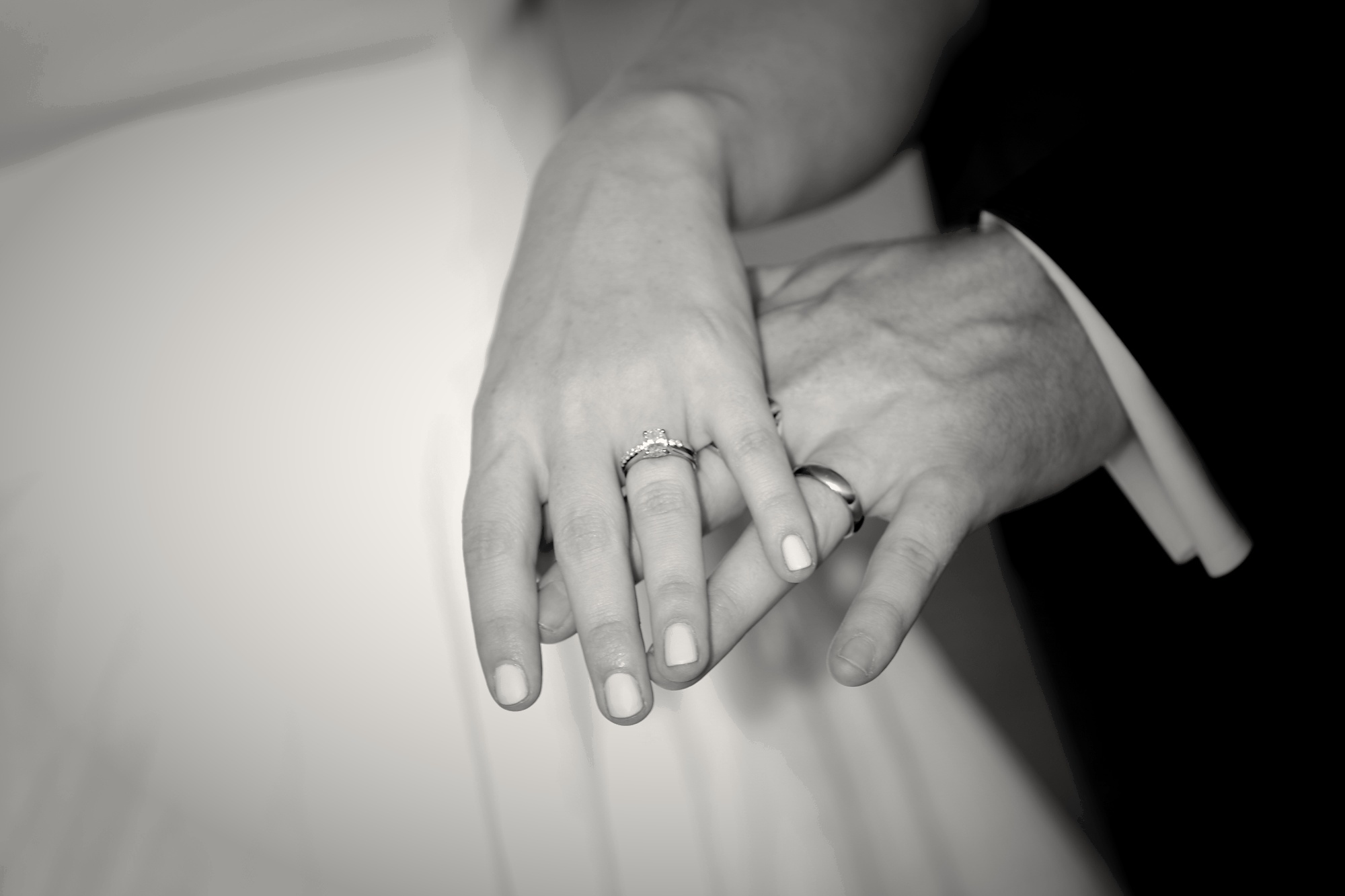 Close-up of bride and groom's intertwined hands showing both wedding rings