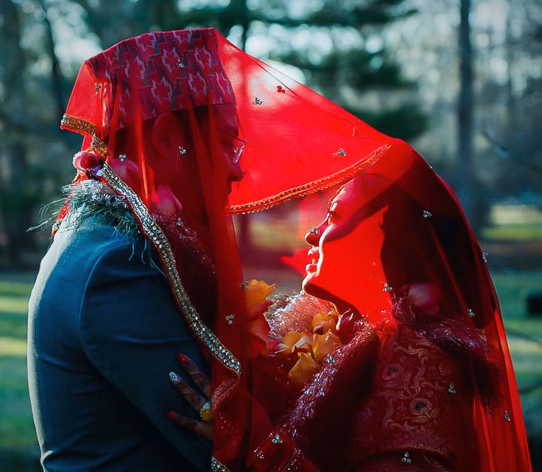 South Asian couple sharing an intimate moment under a red bridal dupatta veil