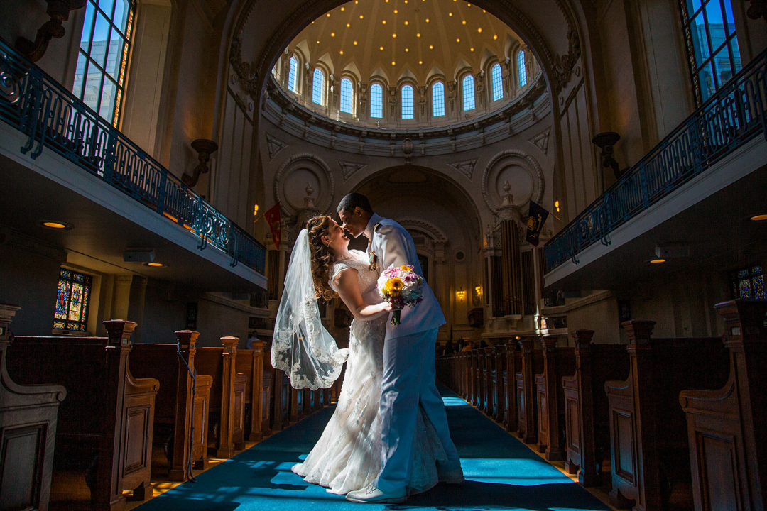 Multicultural couple sharing first kiss in grand chapel aisle — Andrew Rozario Washington DC wedding photographer