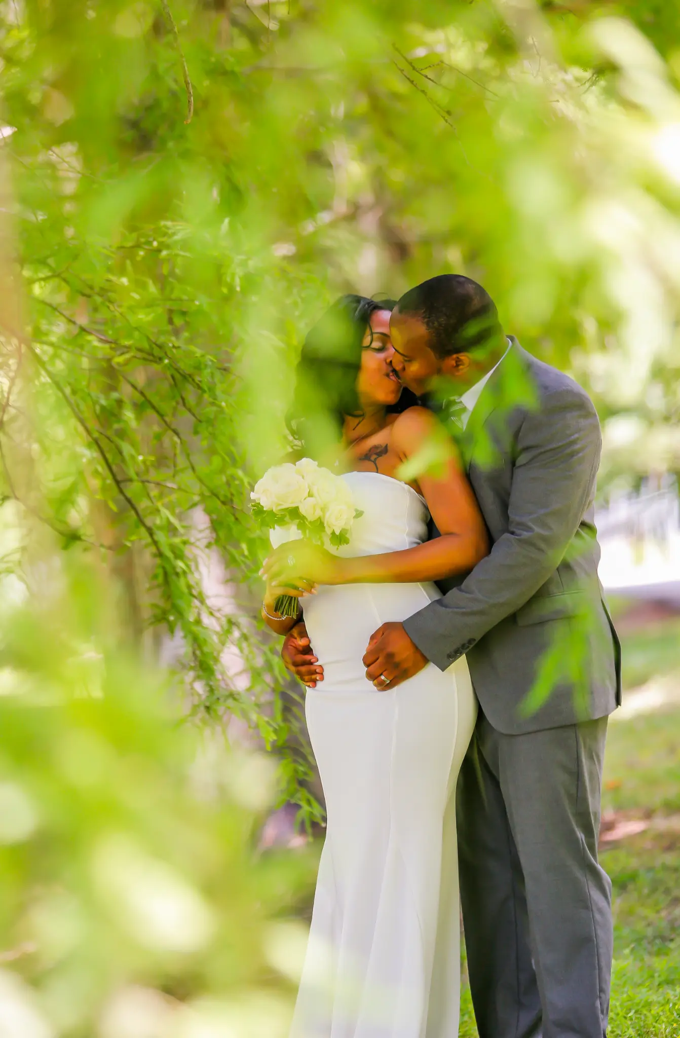 Couple kissing in a garden framed by soft green leaves